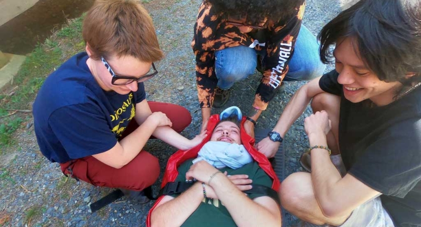A person lays bundled in a stretcher during a wilderness first responder course, while three others brace them. 